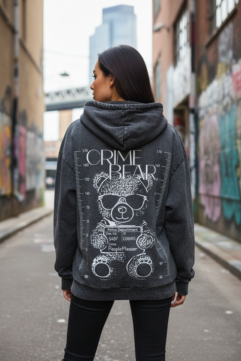 Eine Frau steht in einer städtischen Gasse mit Graffiti-Wänden und trägt den State Your Mind Oversize Washed Hoodie Crime Bear, der einen Bären mit Sonnenbrille und der Aufschrift "CRIME BEAR" sowie nachgemachte Polizeidetails auf dem Rücken zeigt.