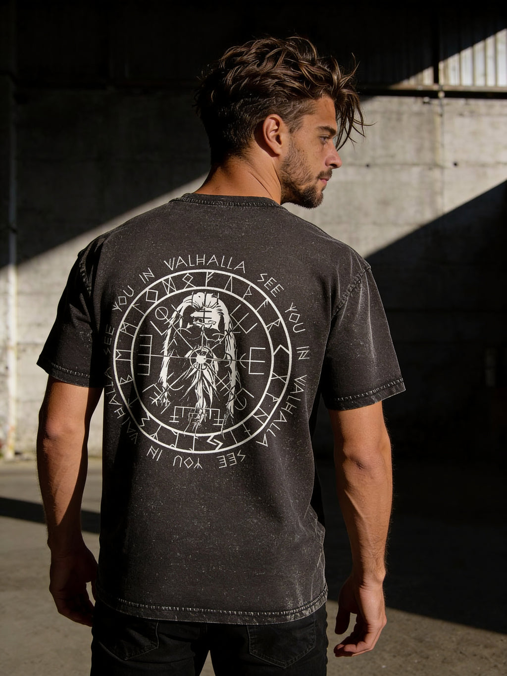 Ein Mann mit kurzen braunen Haaren blickt in die Ferne und trägt das State Your Mind Oversize Shirt Valhalla Brown washed, das eine nordische Grafik mit einem Wikingerkompass Vegvísir und "See you in Valhalla" zeigt. Das Sonnenlicht hebt sein Haar und sein Hemd hervor.