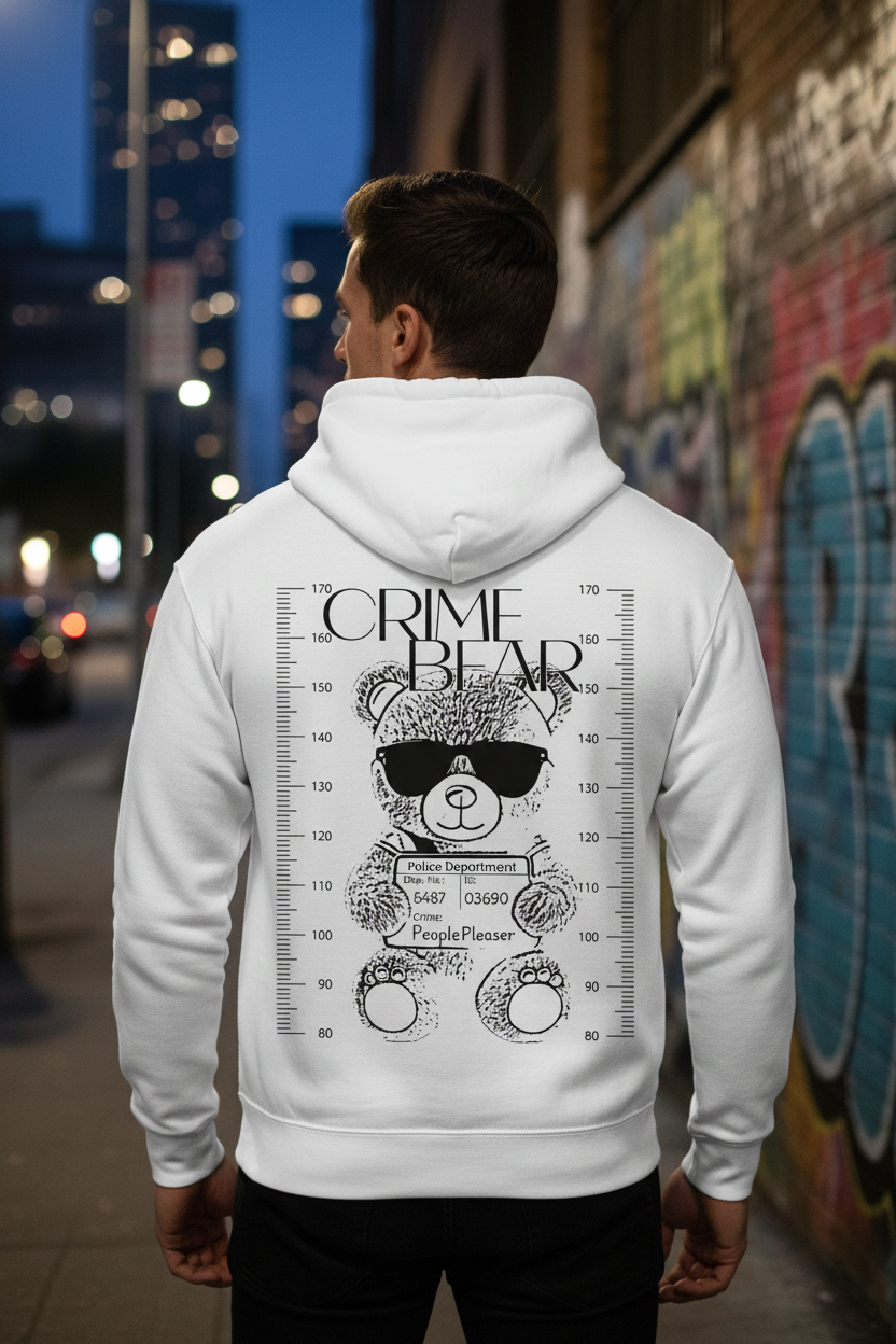 Ein Mann, der einen State Your Mind Zipper Hoodie Crime Bear trägt, auf dessen Rückseite ein markanter Cartoon-Bär mit Sonnenbrille für ein Verbrecherfoto posiert, steht in der Abenddämmerung an einer mit Graffiti bedeckten Stadtmauer.