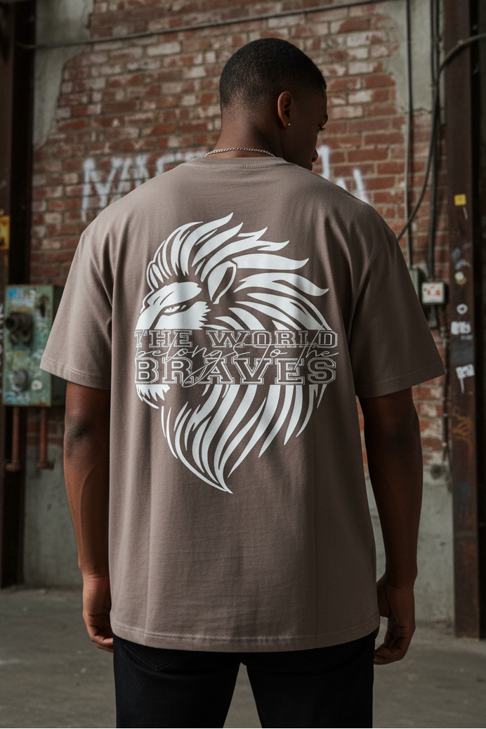 In an industrial scene with brick walls and graffiti, a person is seen from behind wearing the Oversize Shirt Braves featuring a bold Löwen back print and the phrase "THE WORLD BRAVES," highlighting an urban style.
