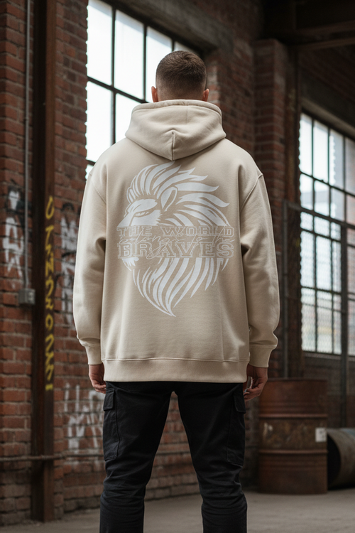 In einem Industrieraum mit Backsteinwänden, großen Fenstern und Graffiti trägt eine Person den State Your Mind Oversize Hoodie Braves mit hochwertigem Baumwollmischgewebe, einem plakativen Löwen-Motiv und "THE WORLD BRAVES" auf dem Rücken.